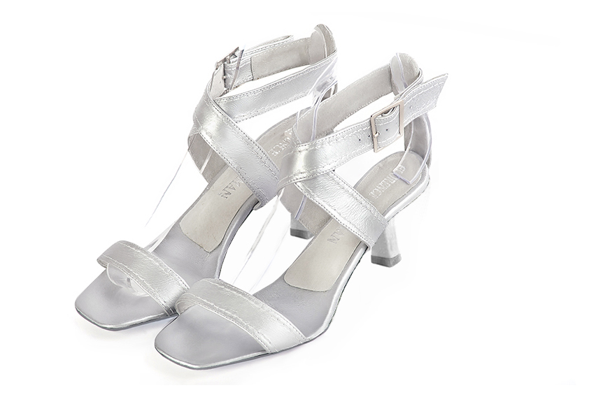 Silver elegant sandals with cross straps across the instep, fully open. Square toe. Medium spool heels.